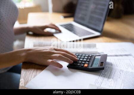 Primo piano donna che usa calcolatrice e computer portatile, controllando i documenti finanziari Foto Stock