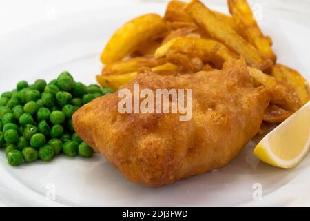 Pesce e patatine con piselli e limone su un piatto bianco primo piano, un piatto tradizionale di cucina inglese o britannica Foto Stock