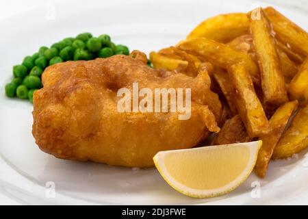 Pesce e patatine con piselli e limone su un piatto bianco primo piano, un piatto tradizionale di cucina inglese o britannica Foto Stock