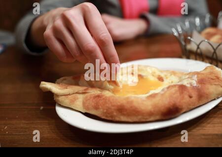 Persona che mangia Adjarian Khachapuri in ristorante georgiano Foto Stock