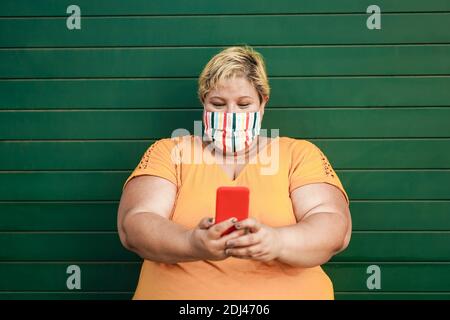 Inoltre, indossa una maschera protettiva per una donna felice che usa lo smartphone - mettere a fuoco sul viso Foto Stock