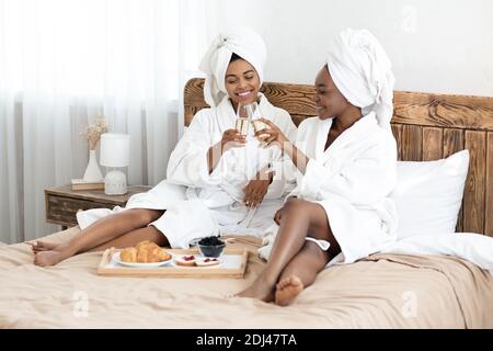Due donne africane con bicchieri di champagne seduti a letto Foto Stock