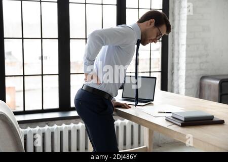 Uomo d'affari malsano che tocca la parte inferiore della schiena, che soffre di mal di schiena in ufficio Foto Stock