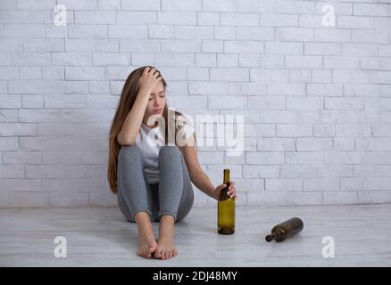 Donna millenaria che si sente depressa, bere alcol per alleviare il dolore emotivo sul pavimento a casa, copia spazio Foto Stock