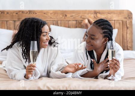 Allegre girlfriends in accappatoi adagiato sul letto e bevendo champagne Foto Stock