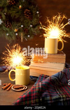 tazze da tè con sfondo brillante e natalizio, tazza in ceramica con luce brillante all'interno, libri e coperta con rotoli e cannella Foto Stock