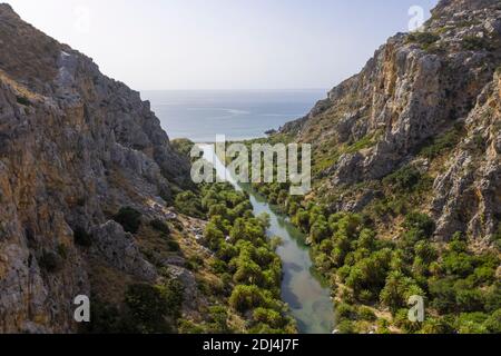 Vista aerea del fiume Kourtaliotis, fiancheggiato da palme, che conduce alla spiaggia di Preveli, Creta, Grecia Foto Stock