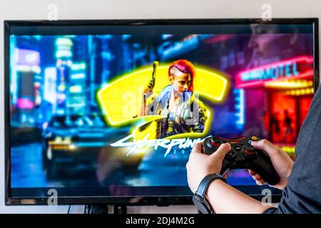 Donna che tiene un controller Red Gear e riproduce video popolari Gioco Cyberpunk 2077 su un televisore e PC Foto Stock