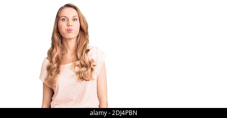 Giovane bella donna caucasica con capelli biondi indossando abiti casual gonfia guance con viso divertente. Bocca gonfia con aria, espressione pazza. Foto Stock