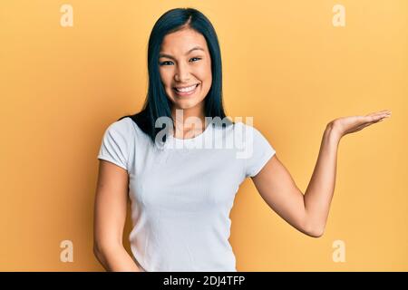 Bella donna ispanica che indossa casual tshirt bianca sorridente allegra presentazione e puntando con palmo di mano guardando la fotocamera. Foto Stock