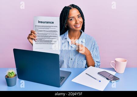 Bella donna ispanica in ufficio mostrando il documento di assicurazione sorridente buon puntamento con mano e dito Foto Stock
