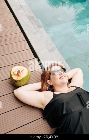 Felice bella donna con cocktail di cocco godendo di sole giorno vicino piscina Foto Stock