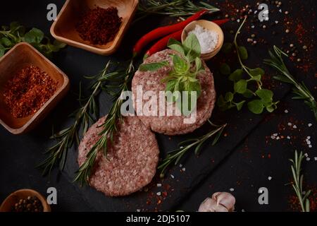 Hamburger di manzo crudo con erbe e spezie. Hamburger crudi su fondo di cemento Foto Stock