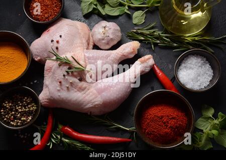 Quarti di pollo crudi, gambe con erbe e spezie pronte per grigliare su sfondo scuro. Foto Stock