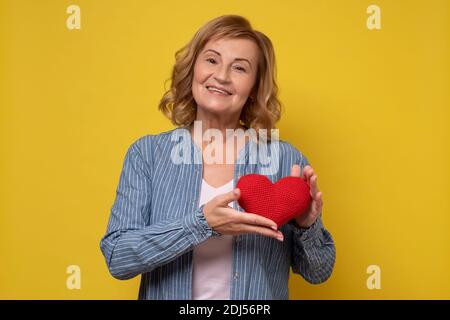 Donna anziana sorridente che mostra il cuore rosso. Concetto romantico. Foto Stock