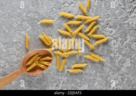 Pasta in un cucchiaio di legno su un tavolo di cemento grigio. Foto Stock