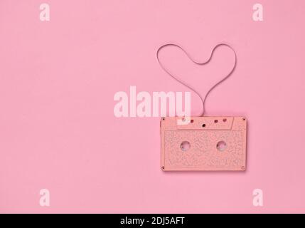 Forma del cuore dal nastro della cassetta audio su sfondo di carta rosa, vista dall'alto. Amore Hipster. Foto Stock