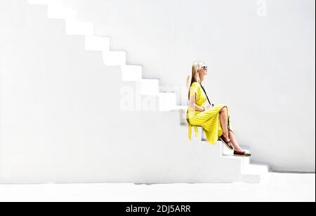 Vista laterale della femmina nella spogliatrice e degli occhiali da sole seduti scala bianca in gesso al sole Foto Stock