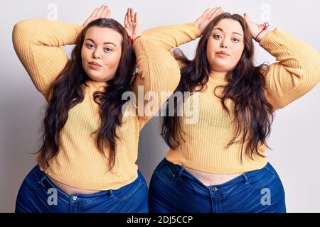 Giovani più taglia gemelli che indossano vestiti casual facendo bunny orecchi gesto con mani palme che osservano cinico e scettico. Concetto di coniglio di pasqua. Foto Stock