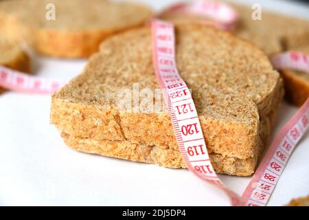 Contro un eccessivo aumento di peso a casa, pane di crusca, fette di pane di crusca e un metro a nastro, Foto Stock