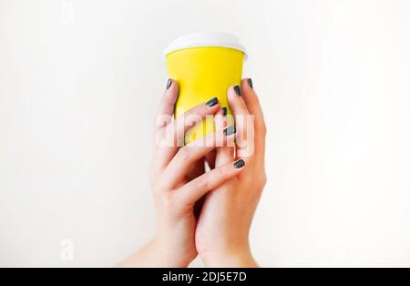 Crop anonimo donna in caldo maglione con manicure scuro che tiene una tazza di caffè usa e getta mentre si riposa a tavola di legno Foto Stock