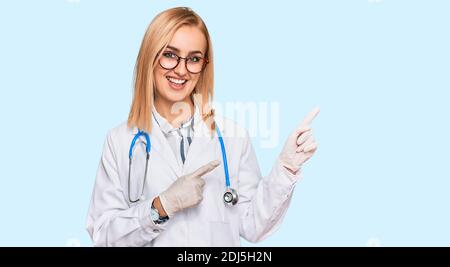 Bella donna caucasica indossando uniforme medico e stetoscopio sorridente e guardando la fotocamera che punta con due mani e dita a lato. Foto Stock