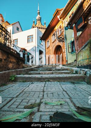 Sighisoara Romania - 11.26.2020: Scena colorata dalle strade acciottolate di Sighisoara con l'iconica Torre dell'Orologio sullo sfondo. Foto Stock