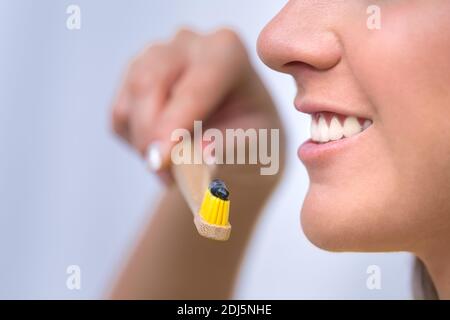 Bella giovane donna sorriso. Donna che tiene eco amichevole spazzolino di bambù naturale con carbone nero sbiancante dentifricio. Salute dentale Foto Stock