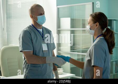 Lavoratore di laboratorio scientifico maschile maturo di successo scuotendo la mano della sua giovane assistente grazioso mentre congratulandosi con lei per lavoro eccellente Foto Stock