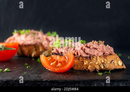 Tostare con pate di maiale, pomodoro ed erbe su ardesia scura Foto Stock