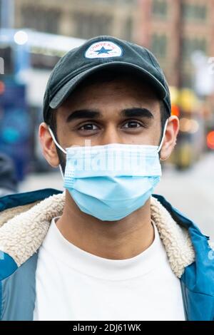 Manchester Dicembre 2020. Un giovane uomo che indossa la sua maschera mentre era in strada, che erano occupati con gli acquirenti e i manifestanti di Natale. Verticale Foto Stock