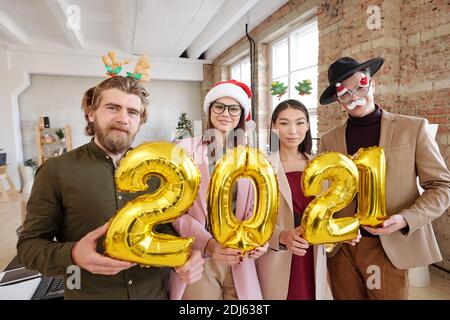 Fila di quattro giovani manager di uffici interculturali felici in Smart casualwear e accessori di natale che tengono i numeri gonfiabili del prossimo anno Foto Stock