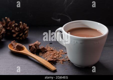 Bevanda al latte al cioccolato presentata con un cucchiaio di legno e cioccolato sbriciolato sul lato e decorata con pineconi. Foto Stock