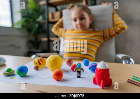 8 anni ragazza studio sistema solare seduta sulla scrivania in camera. Studentessa elementare che fa il suo lavoro - sculta i modelli pianeti da Foto Stock