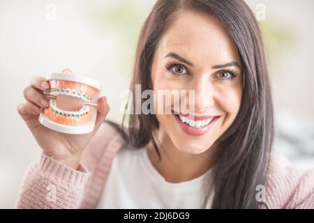 La bruna sorridente tiene in mano un ritratto a denti con bretelle. Foto Stock