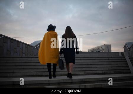 Le ragazze stanno camminando intorno alla città. Le donne in abiti caldi camminano in fondo alla strada la sera. Ragazze dalla parte posteriore. Vita in una città fan. Foto Stock