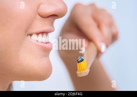 Donna sorridente che tiene lo spazzolino. Primo piano di donna che tiene spazzolino da denti di bambù con dentifricio di carbone nero vicino alla sua bocca. Foto Stock