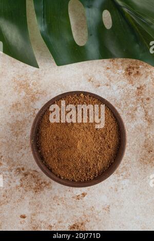 Zucchero di cocco in una ciotola di legno con una foglia di palma. Minimalismo. Il concetto di alimentazione sana. Foto Stock