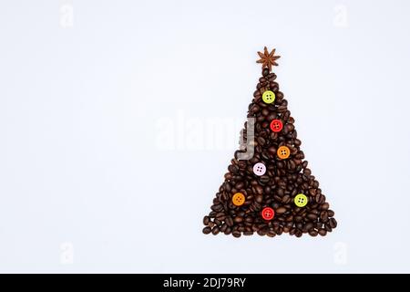 Albero di Natale fatto di chicchi di caffè con stella di anice sulla parte superiore e pulsanti colorati come decorazione. Sfondo natalizio minimo Foto Stock