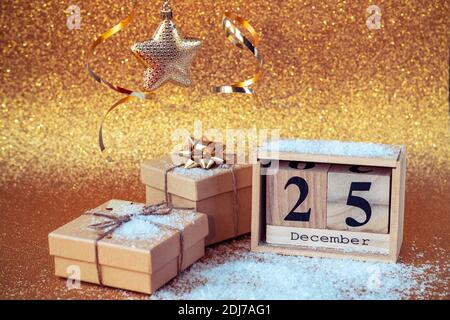 Calendario blocco di legno con data 25 dicembre, decorazioni natalizie e scatole regalo su sfondo dorato con scintille. Foto Stock