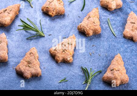 Biscotti fatti in casa a forma di albero di Natale cotti a base di grano integrale e formaggio, aromatizzati con rosmarino su una superficie di pietra blu Foto Stock