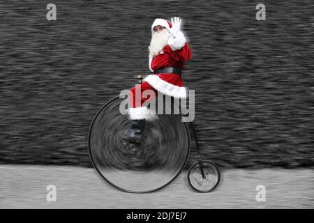 Padre Natale a cavallo di una bicicletta Penny Farthing e ondeggiamento Foto Stock