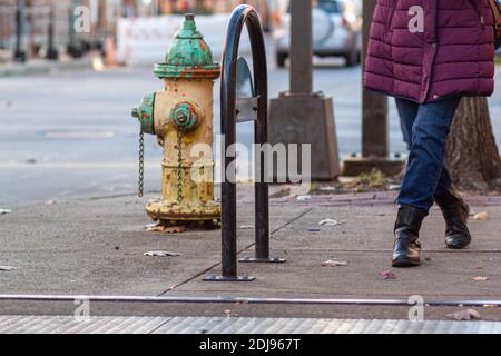 vita giù immagine di una donna che indossa jeans, stivali invernali e spesso giacca viola invernale mentre cammina sul marciapiede in un ambiente urbano. Un'immagine concettuale Foto Stock