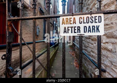 L'area chiusa dopo il cartello scuro sulla piastra metallica è fissata alle ringhiere metalliche di una porta di fronte a un passaggio vintage in un luogo urbano. Uno stretto Foto Stock