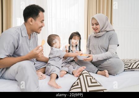 Ritratto di una famiglia felice in abiti piyama. Rilassati mentre gustatevi uno spuntino in camera da letto Foto Stock