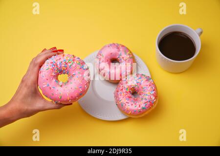 Un primo piano di una femmina che tiene una crema dolce ciambella smaltata su sfondo giallo Foto Stock