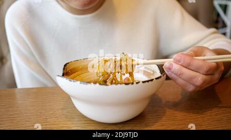 Giovane donna irriconoscibile che mangia tagliatelle trasparenti con frutti di mare in un bar. Foto Stock