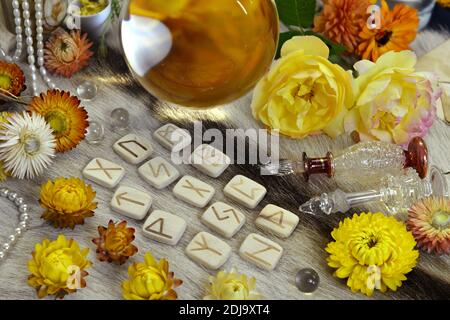 Ancora vita con rune di legno bianco, fiori gialli e sfera di cristallo magico con oggetti rituali sul tavolo delle streghe. Sfondo esoterico, gotico e occulto, Foto Stock