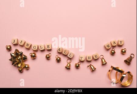 Piccoli blocchi di legno con l'iscrizione Jingle fino in fondo e campane dorate su sfondo rosa, spazio per il testo Foto Stock