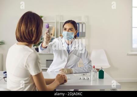 Infermiera in maschera facciale che misura la temperatura corporea della donna senza contatto termometro Foto Stock